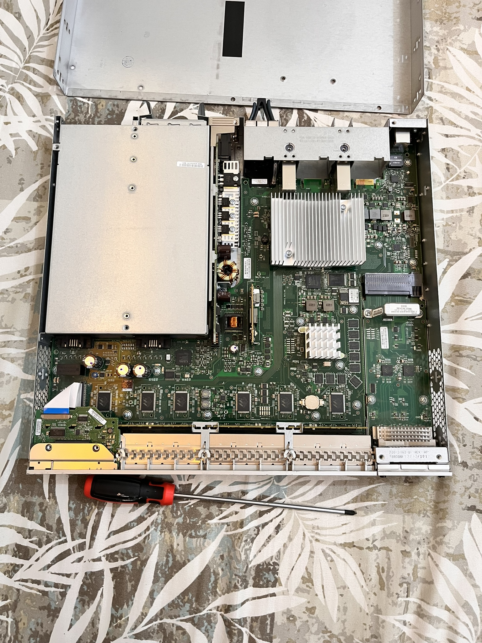 The Cisco 3850 switch opened up, showing its mainboard, heatsinks and power supply, with a screwdriver resting on it.